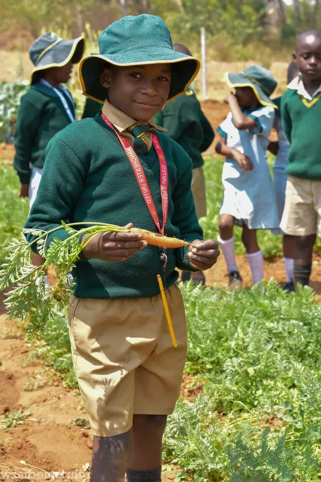 A learner in green uniform and bush hat holds up a carrot